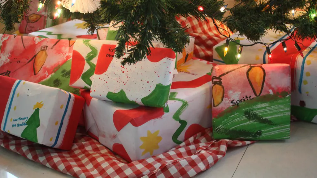 Presents wrapped in hand-painted paper stacked under a lit Christmas tree on a red and white checked tree skirt