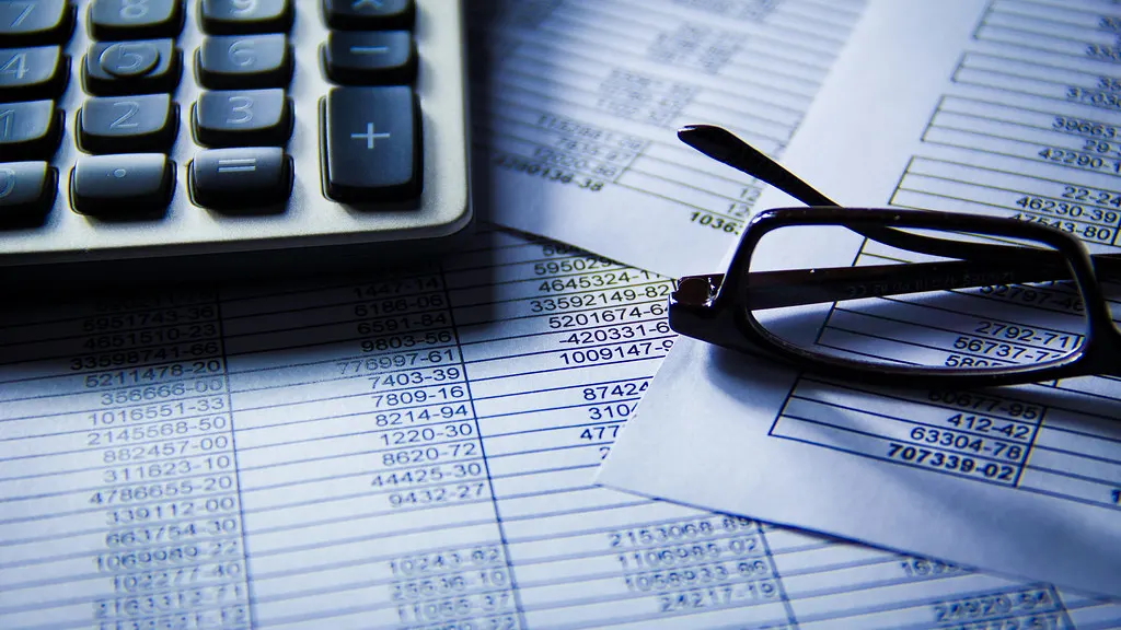 A calculator and reading glasses resting on printed columns of figures