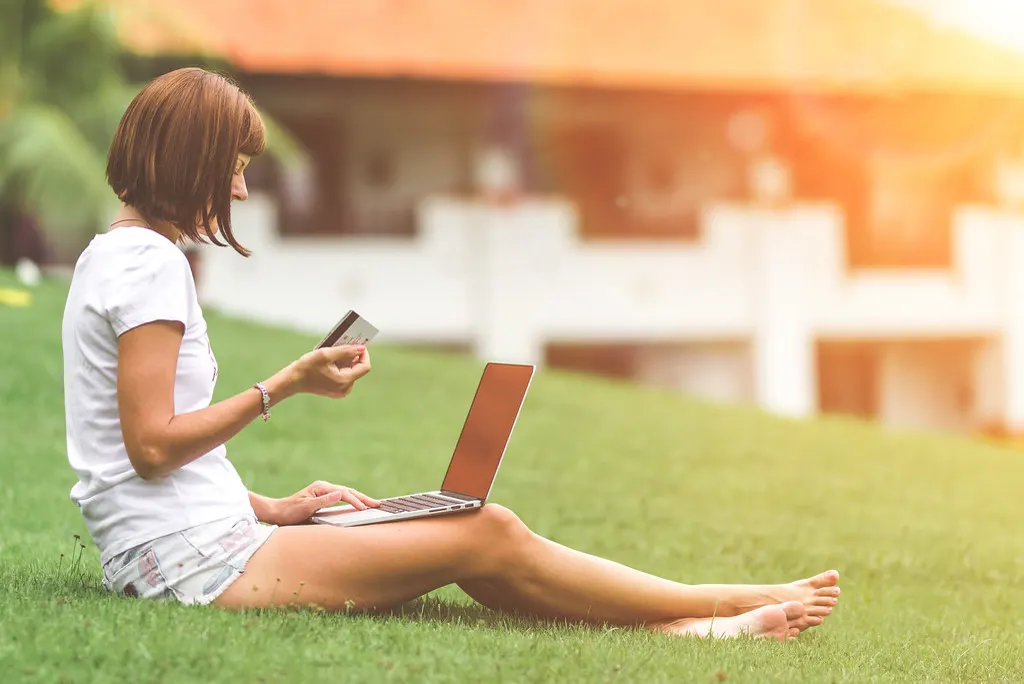 A woman sitting on a lawn with a laptop, holding a payment card