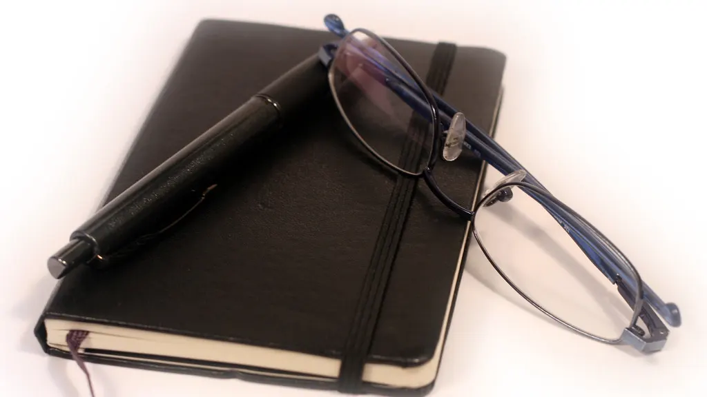 A black notebook with a pen and a pair of reading glasses resting on it