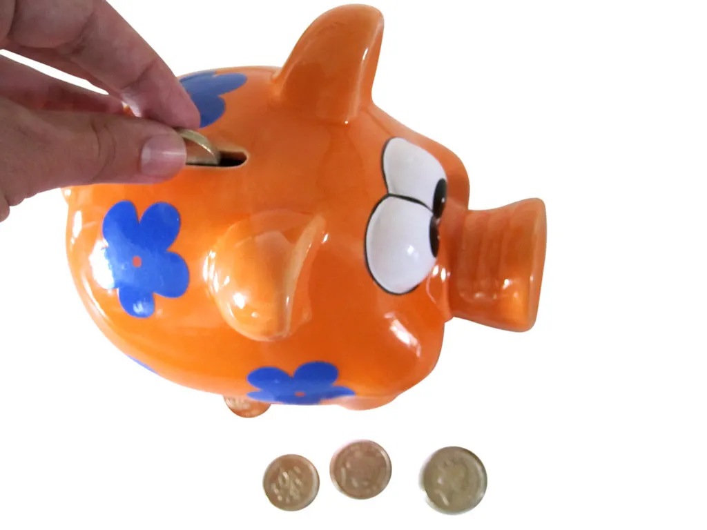 A hand dropping a coin into an orange piggy bank
