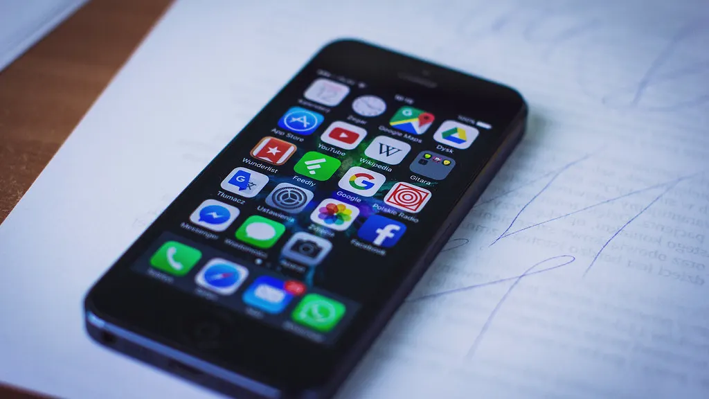 A smartphone home screen full of app icons, lying on a sheet of paper