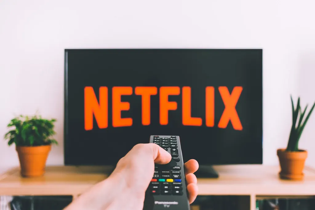 A hand pointing a remote at a television showing the Netflix logo