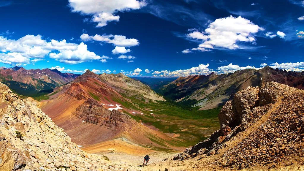 A hiker on a rocky trail looking out over colourful mountains under a blue sky